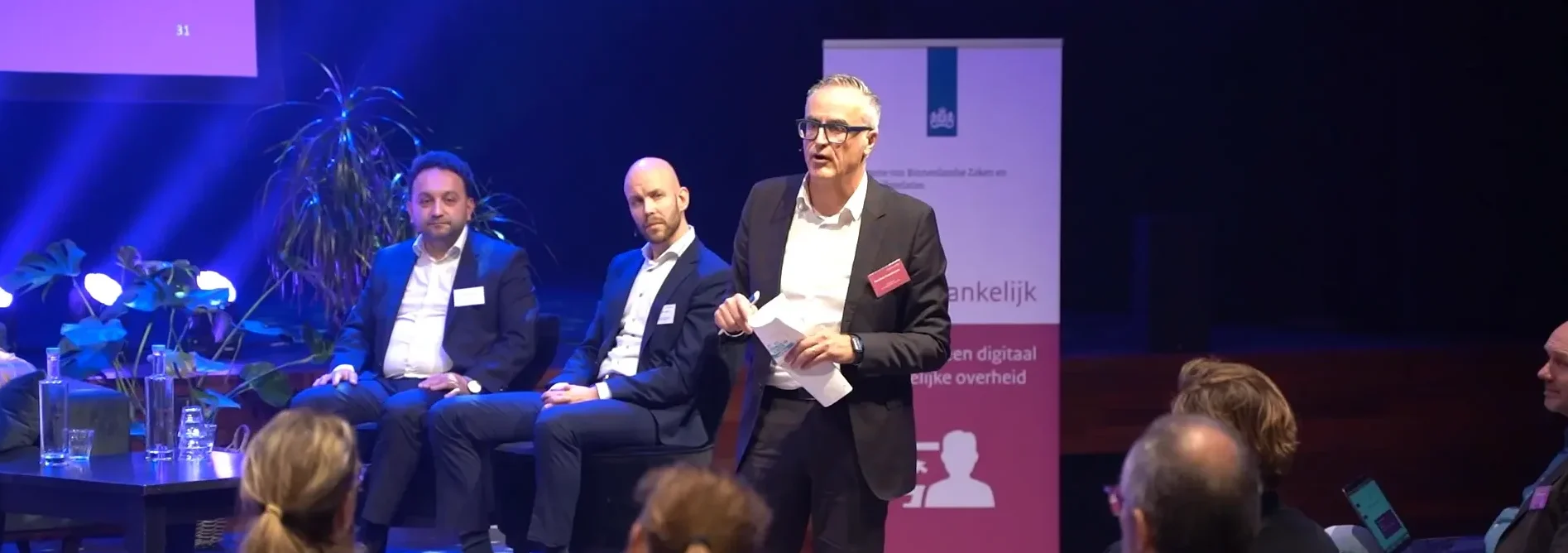 Manfred Rosenboom staat op een podium. Hij vat de middag samen aan het einde van de roadshow DigiToegankelijk in Amersfoort.